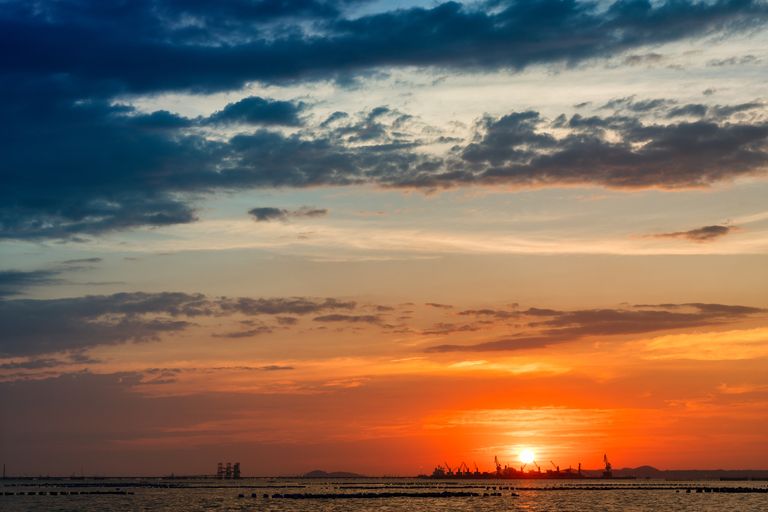 Epic sunset view over the sea with silhouettes of industrial cranes on the horizon.
